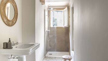 Une salle de bain équipée d’un lavabo, d’un miroir, d’une douche et d’un tabouret.