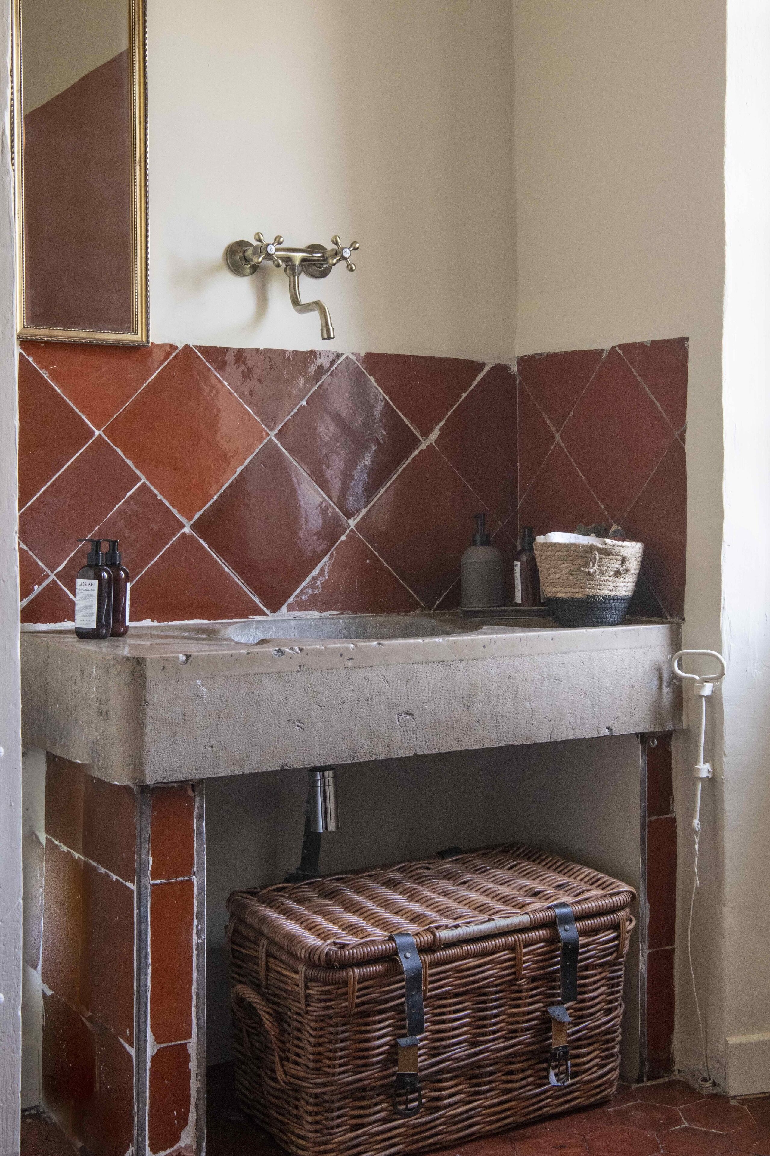 Un baño con pared de azulejos, un lavamanos y una cesta de mimbre.
