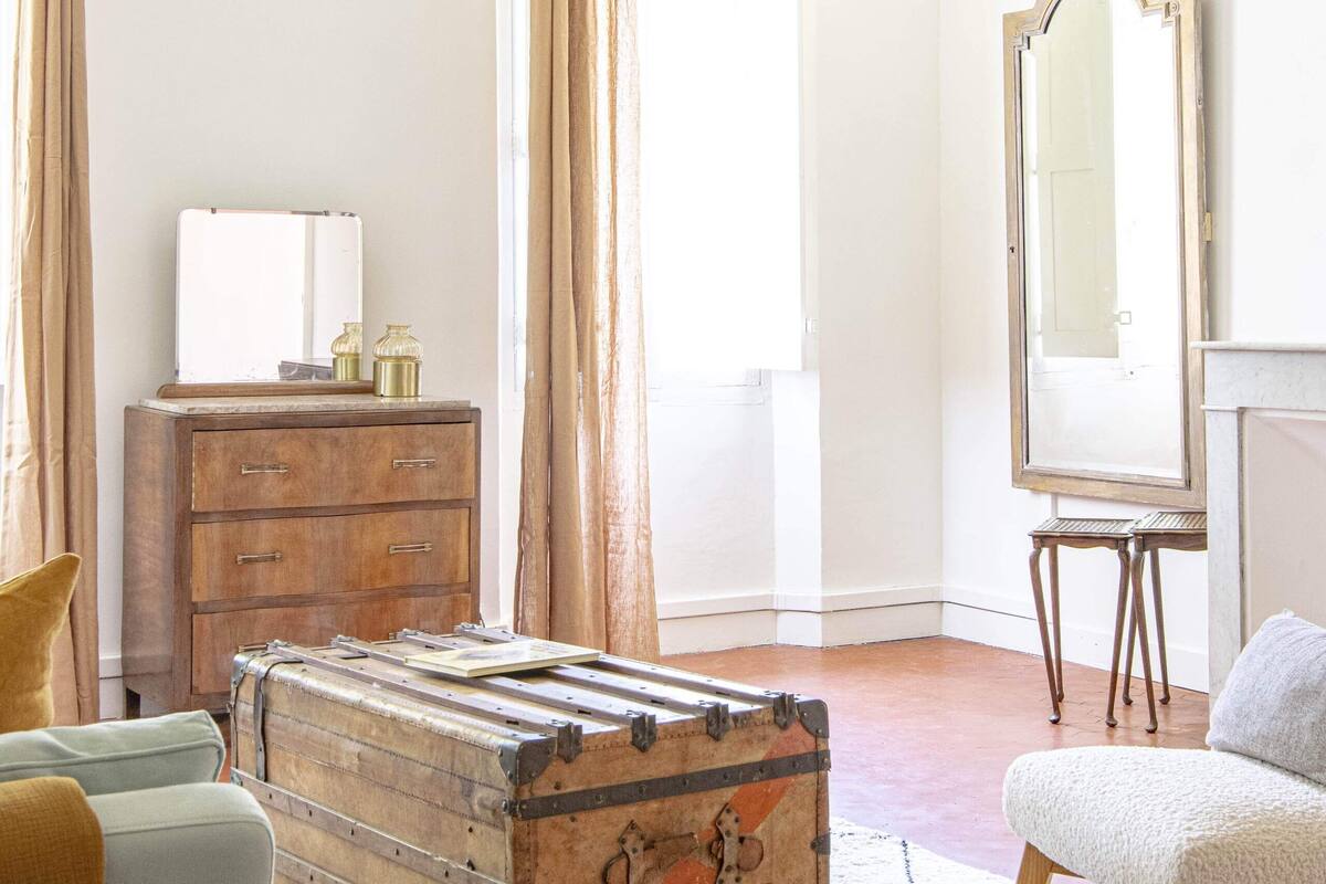 A room with a vintage suitcase, a wooden dresser, a mirror, and a chandelier.