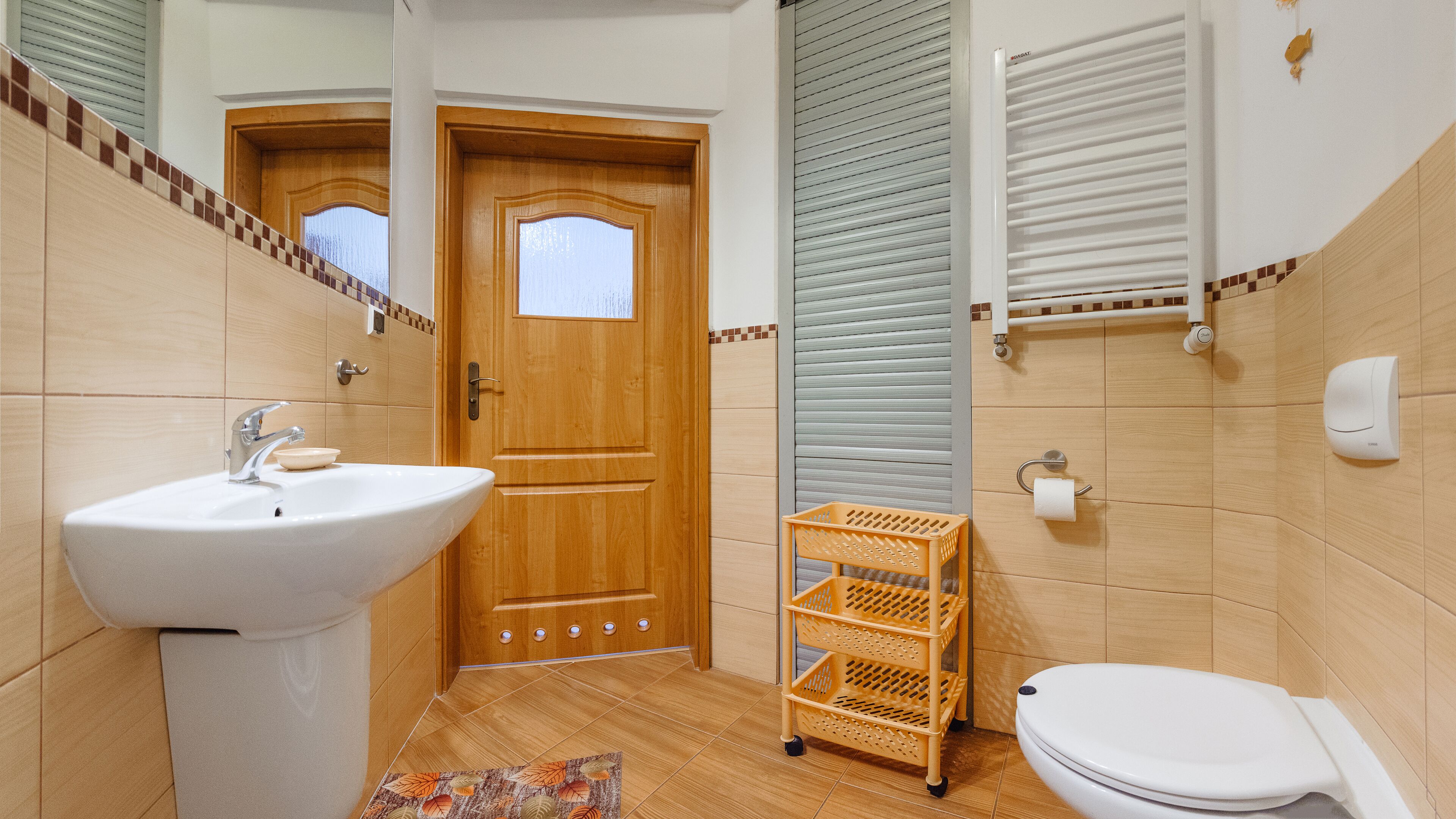 A bathroom with a wooden door, a white sink, a toilet, and a small shelf.