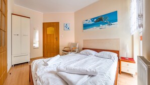 A neatly made bed with white linens, a wooden wardrobe, a chair, and a painting of a tree on the wall. - Apartamenty Sun&Snow Rezydencja Bursztyn (Swinoujscie)