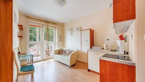 A modern apartment with a dining area, a sofa, a kitchenette, and a balcony with a view of greenery. - Apartamenty Sun&Snow Rezydencja Bursztyn (Swinoujscie)