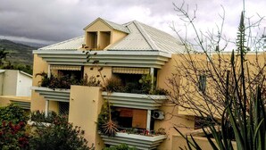 A two-story building with a flat roof, balconies with plants, and a large cactus in the foreground. - Corail de l Ermitage Duplex T3 5mn beach (Saint Paul)