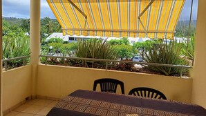 A balcony with a striped awning, a table with a patterned tablecloth, and chairs. - Corail de l Ermitage Duplex T3 5mn beach (Saint Paul)