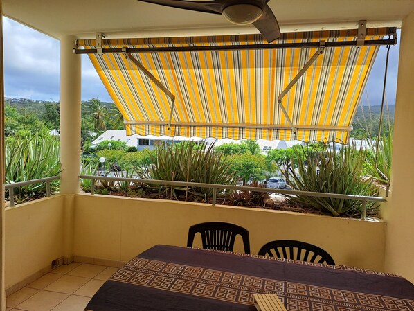 A balcony with a striped awning, a table with a patterned tablecloth, and chairs.