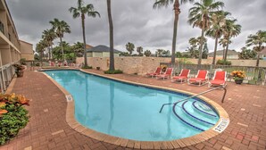 Ein Pool mit roten Liegestühlen, Palmen und einem Pflasterweg.