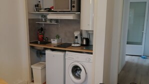 Une cuisine compacte équipée d’un four à micro-ondes, d’une machine à café et d’un lave-linge.