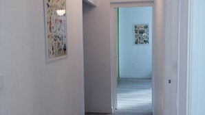Un couloir aux murs blancs, doté d’un plancher en bois et d’un luminaire au plafond. Deux œuvres d’art encadrées ornent les murs.