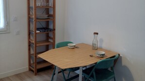 Un coin repas avec une table en bois et des chaises de couleur turquoise, une étagère en bois et un mur blanc.