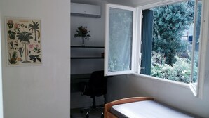 Une chambre avec un lit en bois, une fenêtre avec des rideaux, un bureau avec une chaise et un climatiseur fixé au mur.