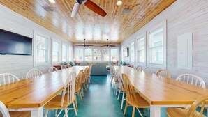 Une pièce spacieuse avec une longue table en bois et des chaises, un ventilateur de plafond et de grandes fenêtres.