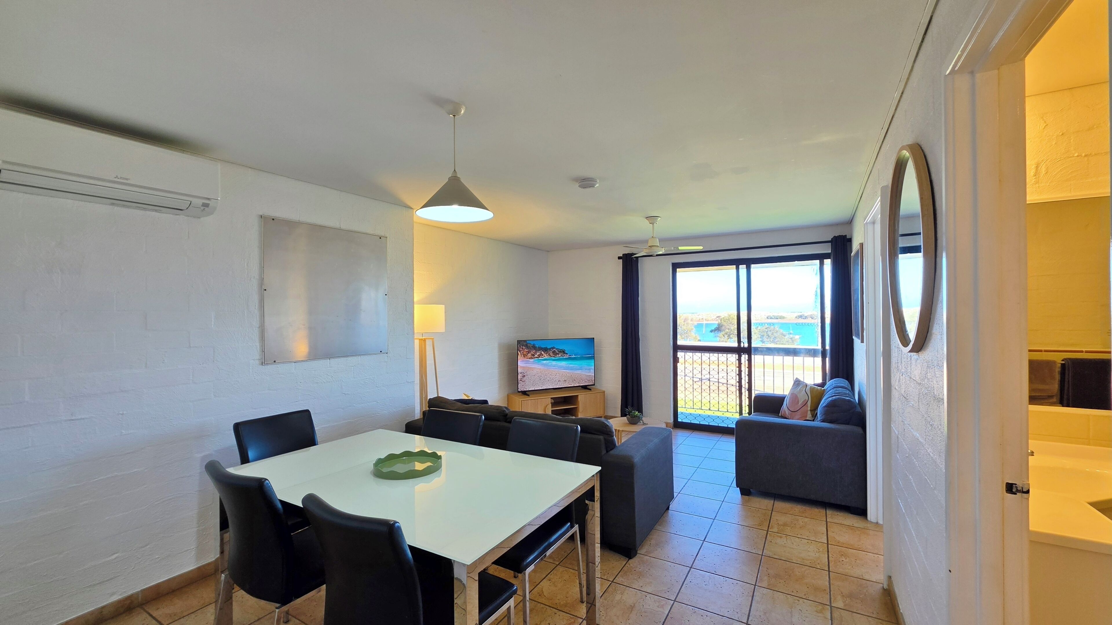 A compact living space with a dining area, a sofa, a TV, and a balcony with a view.