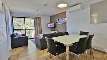 A modern dining area with a white table and black chairs, a grey sofa, and a TV on the wall.