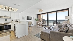 A modern kitchen with white cabinetry, a built-in oven, and a dining area with a round table and chairs. - 🏖️Oceanfront Sunrise Overlooking Pool!  Car Free Beach, Walk to shopping & dining! Sunrise 805 (New Smyrna Beach)