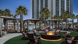 A poolside area with lounge chairs, a fire pit, and a view of a high-rise building. - Re-decorated Ocean View Unit-Full Access-605B (Myrtle Beach)