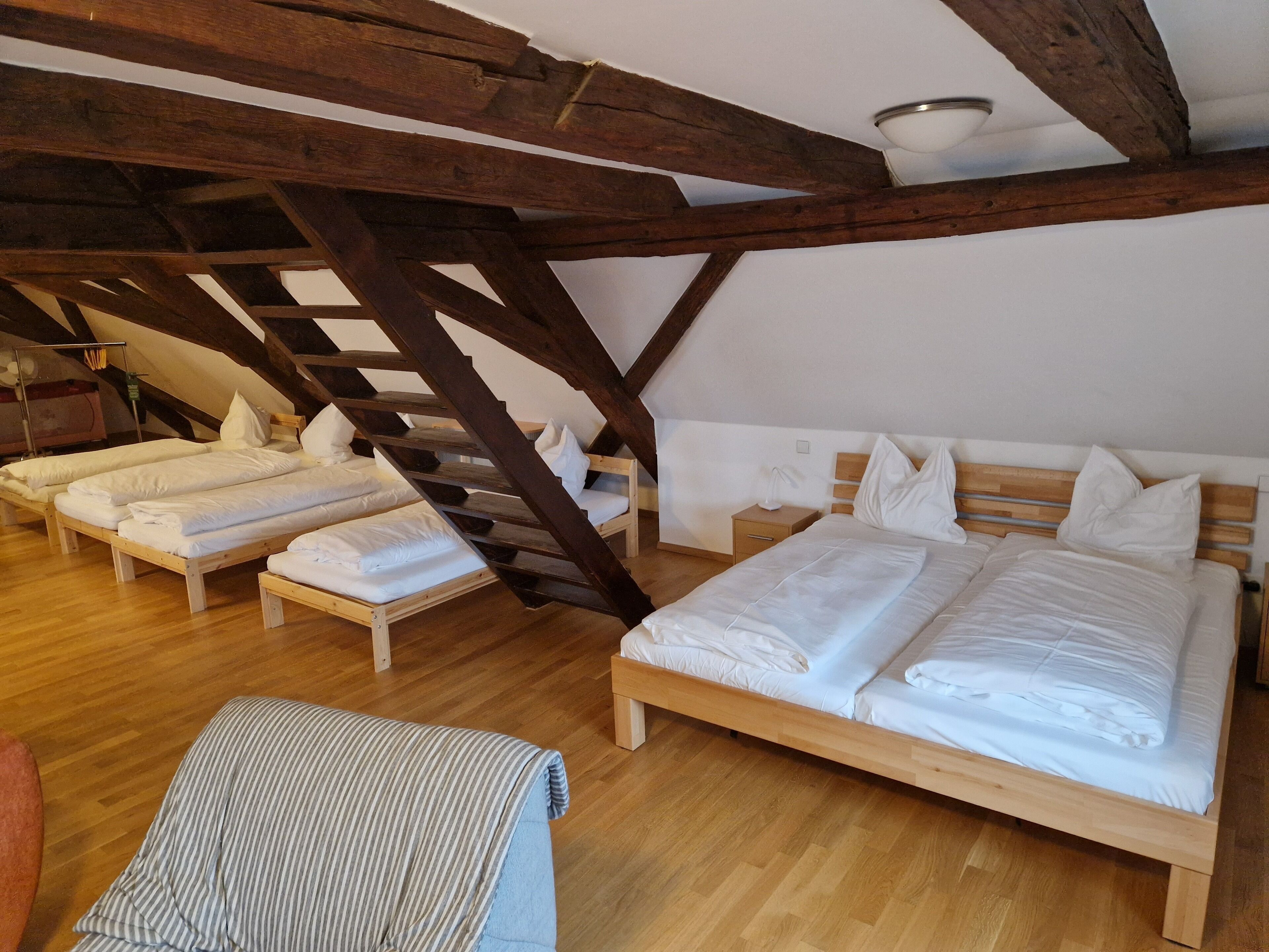 A room with four wooden beds arranged in a row, a wooden staircase, and a wooden floor.