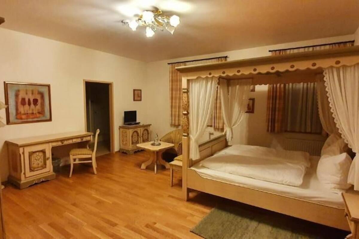 Quarto com cama de dossel, uma escrivaninha e uma cadeira.