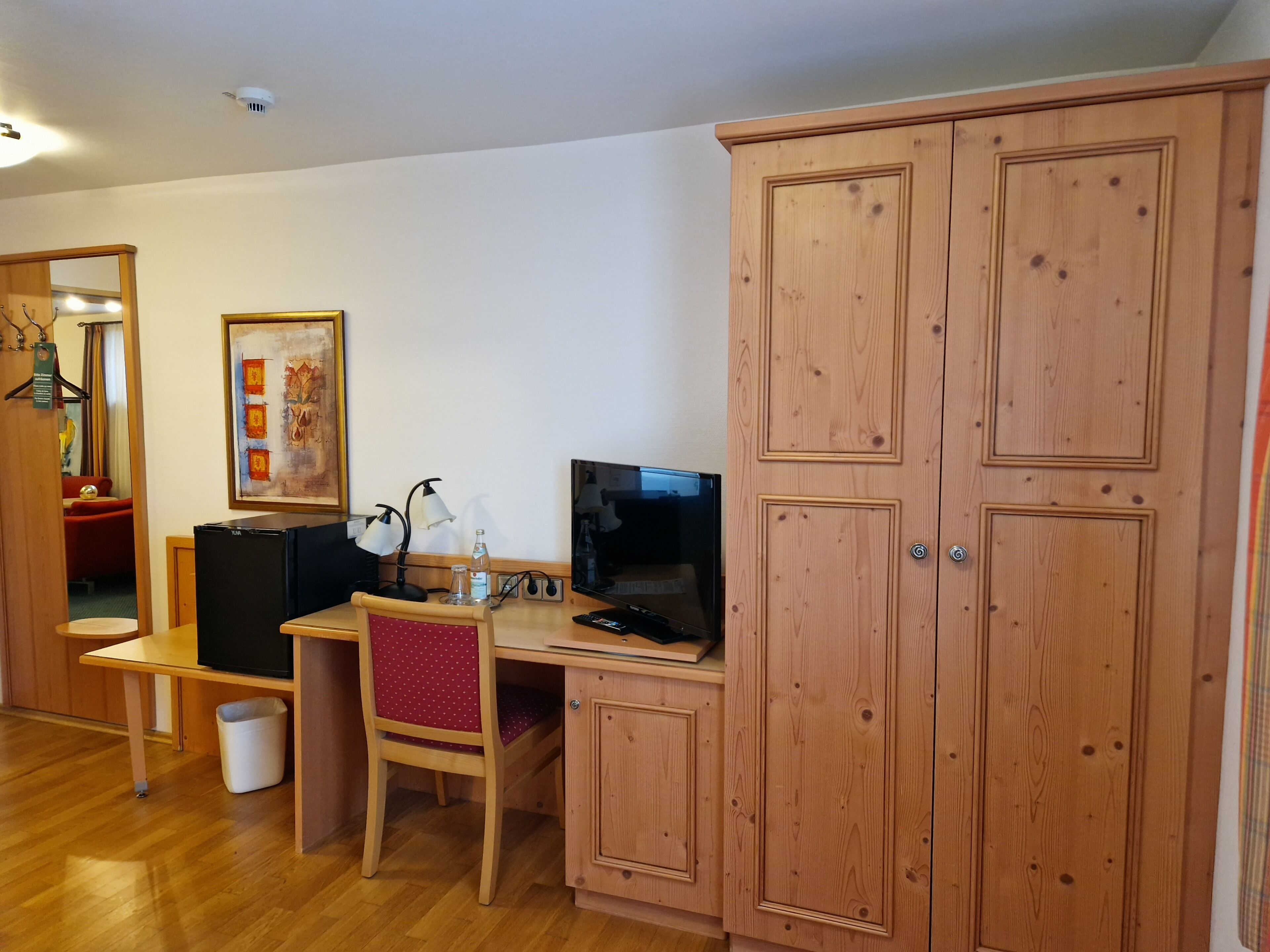 Een compacte, goed verlichte kamer met een houten bureau, een stoel, een televisie en een kast.