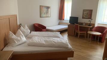 Habitación de hotel con una cama de madera, un escritorio con una computadora, una silla y una mesita.