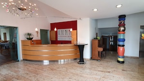 A reception area with a wooden reception desk, a sign for 'SCHIERHUBER Restaurant | Bar', a chandelier, and a tall decorative pillar.