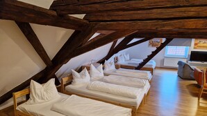 A room with four wooden beds arranged in a row under a sloped ceiling with exposed beams.