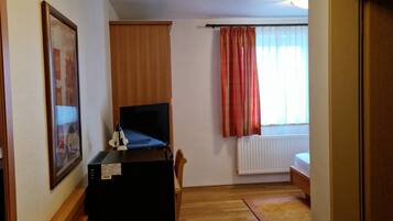 A room with a wooden desk, a television, a radiator, and a window with curtains.