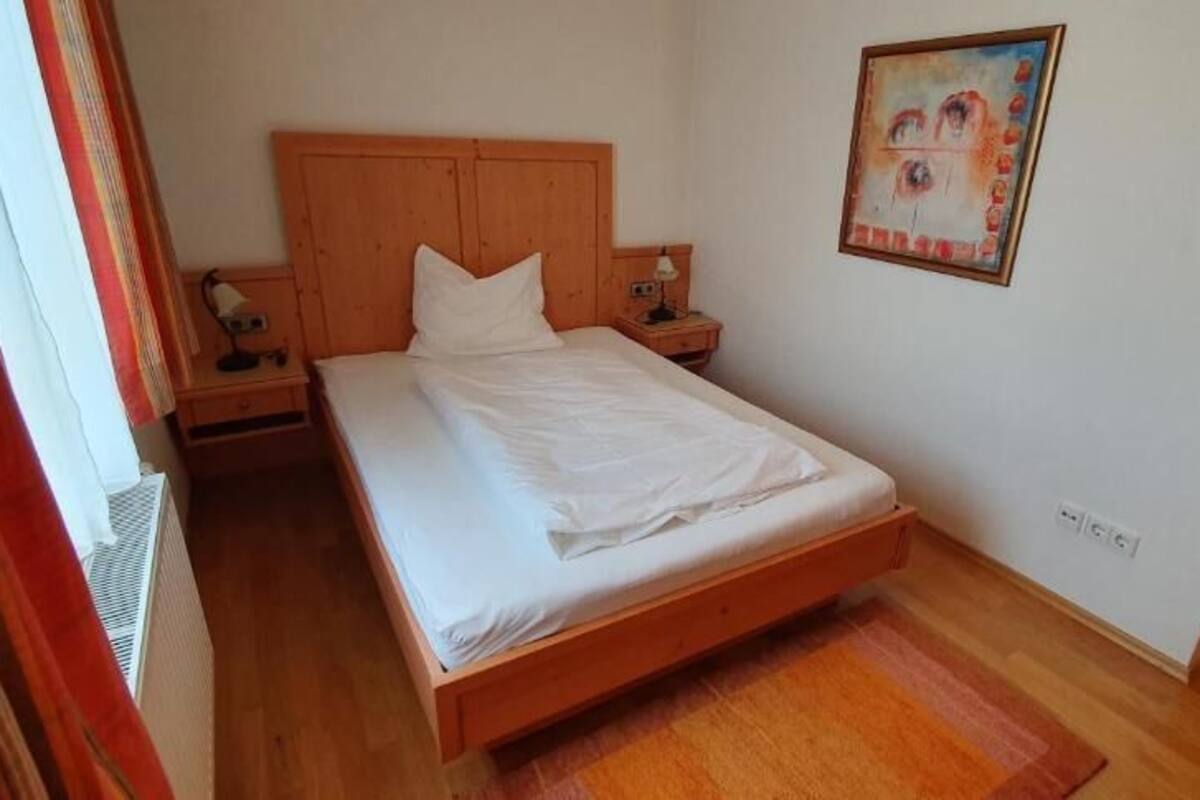 Quarto com cama de madeira, mesa de cabeceira, relógio de parede e quadro emoldurado.