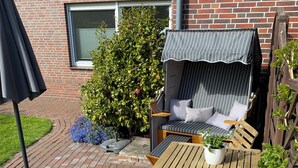 A patio with a wooden table and chairs, a cushioned bench, and a grill area.