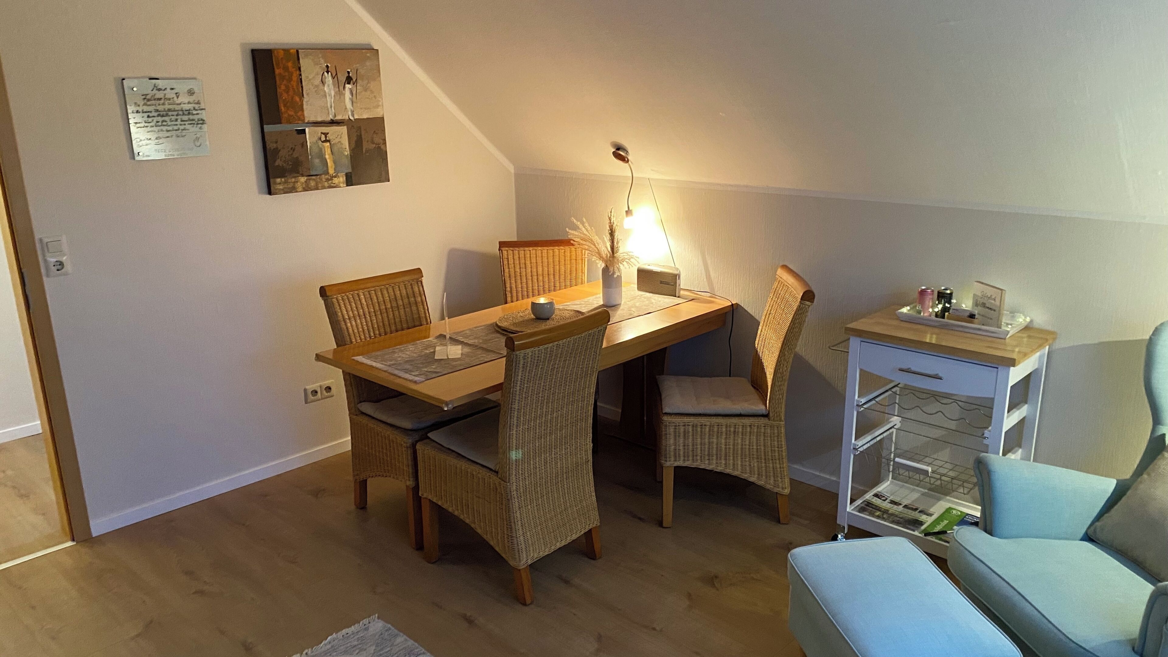 Un coin repas avec une table en bois, des chaises en osier et une petite table d’appoint sur laquelle se trouve une lampe.