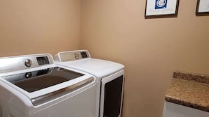 A laundry room with two stacked washers and dryers, a towel rack, and framed artwork on the wall.