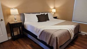 A neatly made bed with white and brown bedding, two bedside lamps, and a window with blinds.
