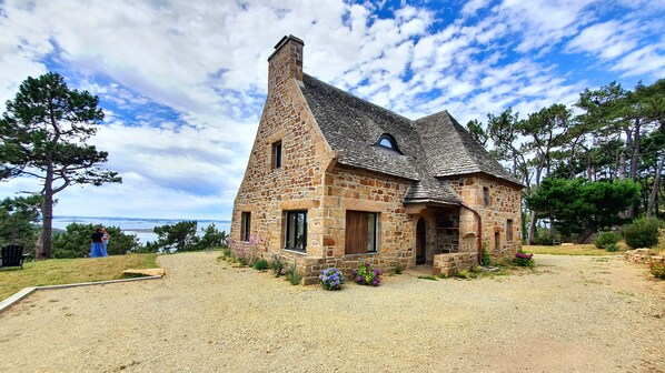 Una casa de piedra con techo inclinado, chimenea y vista al mar.