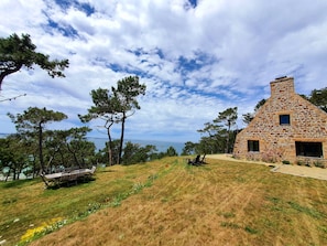 Una cabaña de piedra con chimenea, rodeada de césped y árboles.