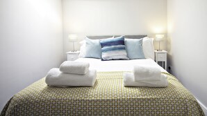Ein ordentlich gemachtes Bett mit weiß-blauen Streifen-Kissen, einer grün gemusterten Tagesdecke und zwei gefalteten weißen Handtüchern auf dem Bett.