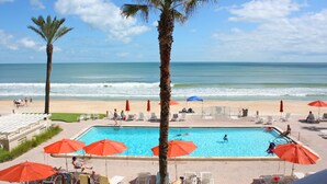Un espace piscine offrant une vue sur la plage et l’océan, entouré de palmiers et de chaises longues.