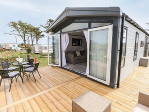 A modern, compact mobile home with a glass door leading to a living area, furnished with a sofa and a coffee table. - Puffin Lodge (Haverfordwest)