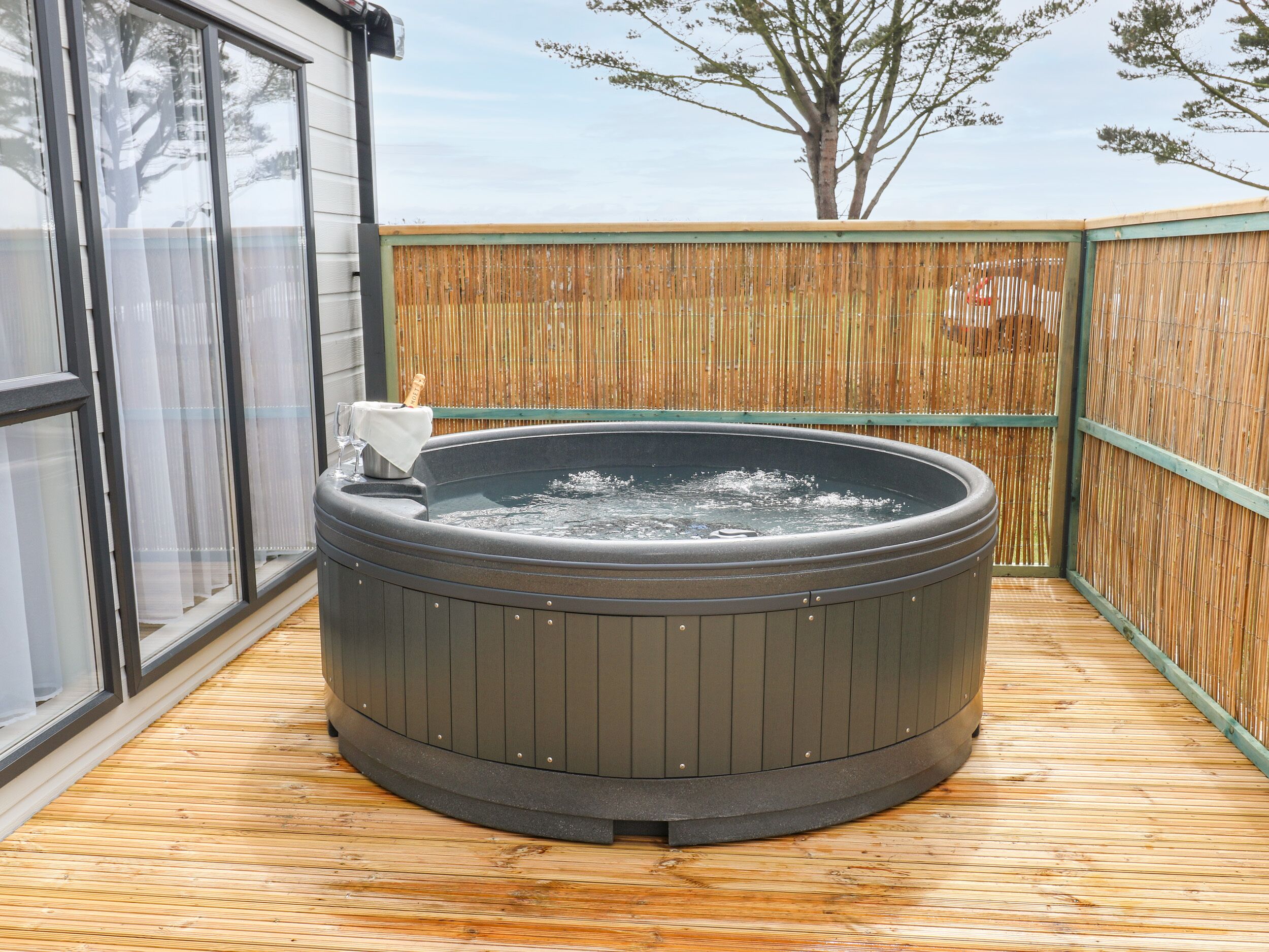 A hot tub on a wooden deck with a bamboo fence in the background.