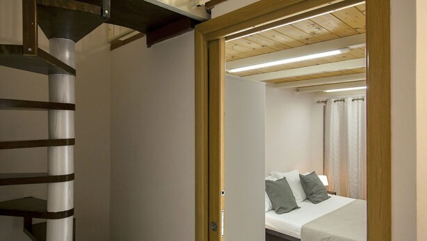 A bedroom with a bed, pillows, and a wooden ceiling.