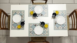 A dining table with four plates and four cups, each with a patterned table runner.