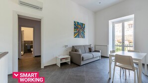 Een moderne woonkamer met een grijze bank, een witte eettafel en een schilderij aan de muur.