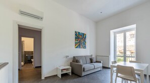 Uma sala de estar moderna com um sofá cinzento, uma mesa de jantar branca e um quadro na parede.