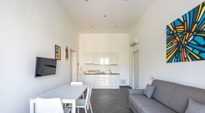 Um espaço de estar moderno com área de jantar, um sofá cinzento e uma cozinha ao fundo.