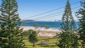 A coastal view with a beach, walking paths, and a distant city skyline.