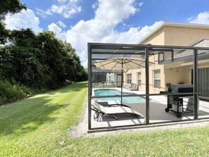A glass-enclosed outdoor pool area with lounge chairs and a barbecue setup.