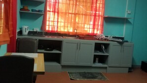 Eine kleine Küche mit türkisfarbenen Wänden, einem Fenster mit orangefarbenen Vorhängen und einem Deckenventilator.
