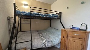 Ein Stockbett mit gemustertem Bettbezug, ein Nachttisch aus Holz mit Griff und eine Wandleuchte.