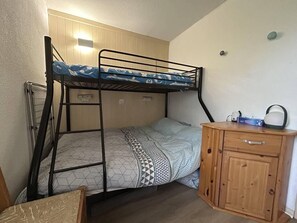 A bunk bed with a patterned bedspread, a wooden cabinet with a handle, and a wall-mounted light fixture. - 100m from ski slopes, 2nd floor, view mountain, balcony, ski locker, 28m², Valmorel (Valmorel)