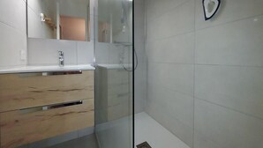 Ein modernes Badezimmer mit Duschkabine aus Glas, weiß gefliesten Wänden und einem hölzernen Waschtisch mit Spiegel.