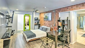 A modern bedroom with a bed, desk, chair, and a brick accent wall.