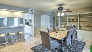 A modern kitchen with a dining area, featuring a wooden table, bar stools, and a ceiling fan.